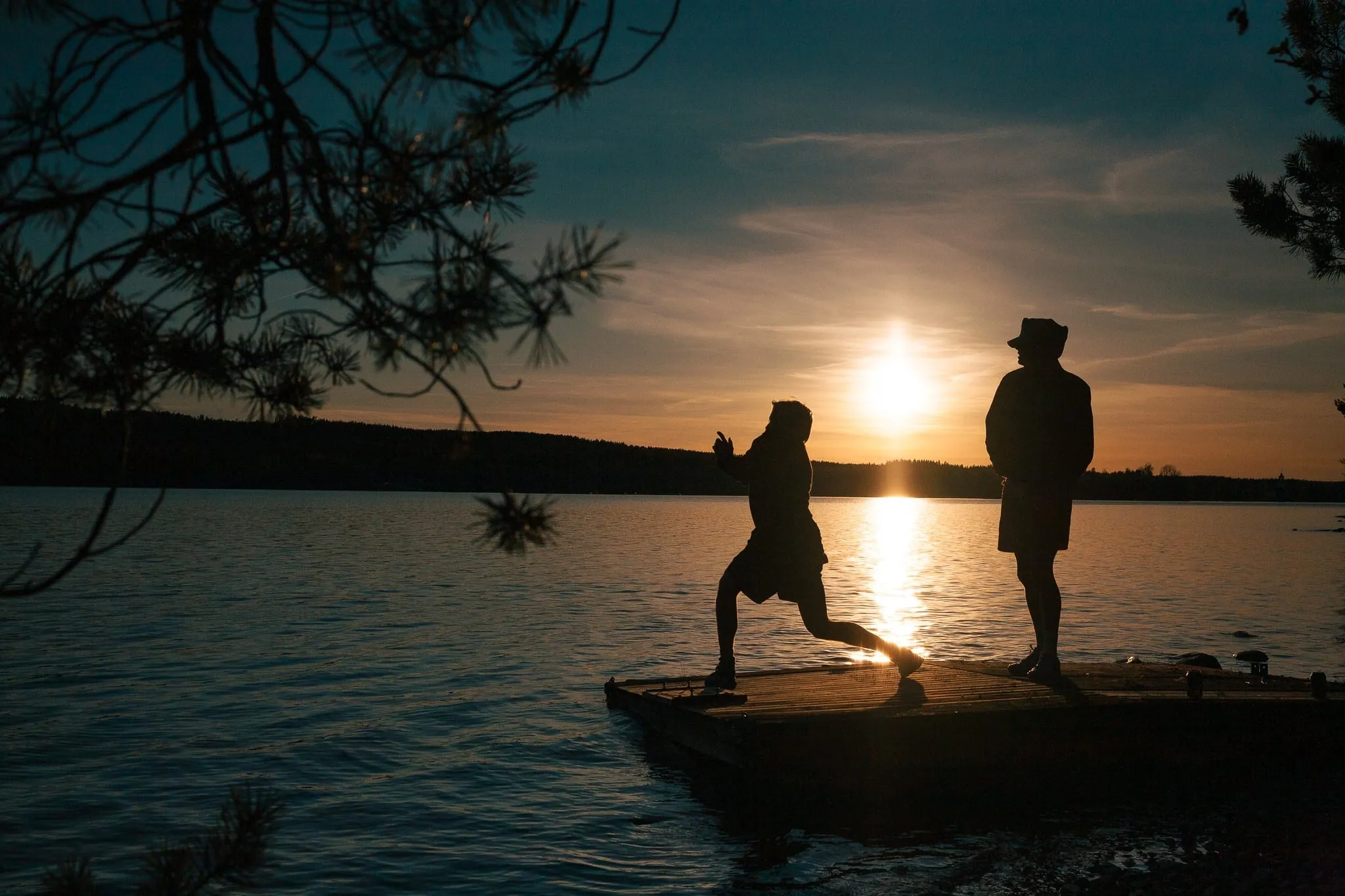 Two people on a jetty silhouetted against a summer sunset over a lake