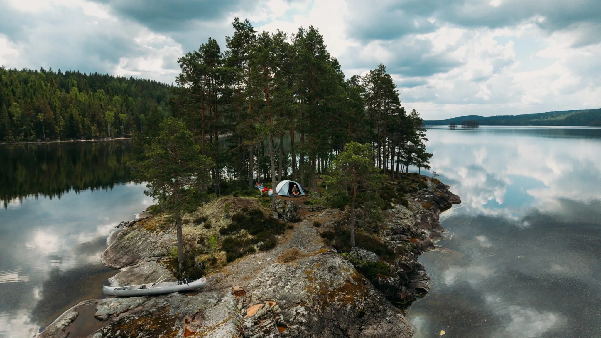 Aerial view of a tent and canoe on a small rocky island in a calm lake